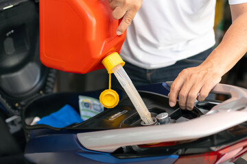 Man filling up fuel into Motorcycle tank with gasoline from spare tank. canister of 5 liters,...