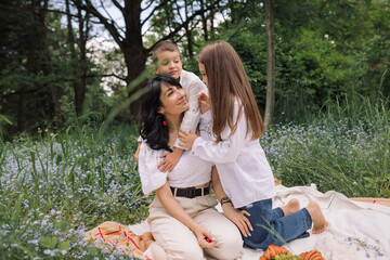 Brother and sister having fun and cuddling with mom at a picnic in the park. Family time outdoors.
