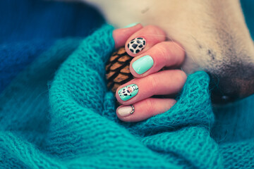 Dog nose and minty nail design closeup. Funny decorations on fingernails, bright colors, knitted sweater pattern. Selective focus on the details, blurred background.
