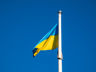 The blue and yellow Ukrainian flag flying in the sky on the flagpole in sunlight. The national flag of Ukraine has two equally sized horizontal bands of blue and yellow