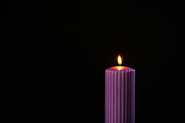 Purple candle with orange flame over black background