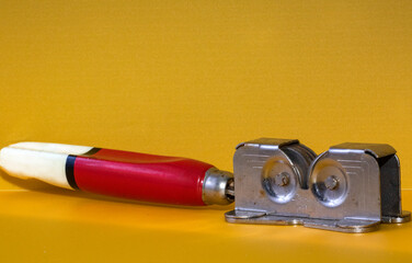 Close up of a retro old knife sharpener with a red and white colored wooden handle on yellow background