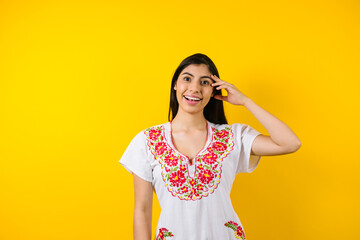 portrait of young latin woman with mexican dress and copy space on yellow background in Latin America	