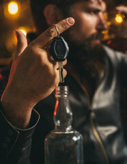 Drunk and hangover driver with car key in alcoholism problem and alcohol abuse concept. Man with beard holds glass of brandy.