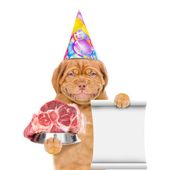 Smiling puppy wearing a party cap holds bowl with raw meat and shows empty list. isolated on white background