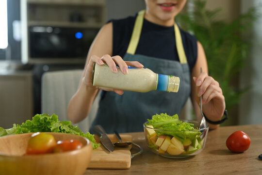 Young Housewife Pouring Sauce  From Bottle Into Vegetable Salad.