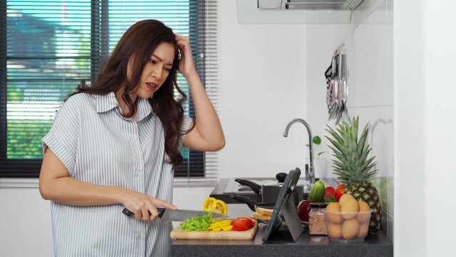 stressed woman cooking and preparing vegetables according to a recipe on a tablet computer in the kitchen at home