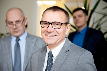 Portrait of smiling confident senior businessman standing with people of team in background