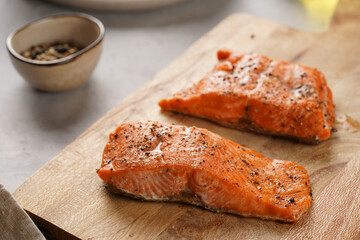 Two grilled fish steaks - red salmon on wooden board, olive oil, avocado on grey background