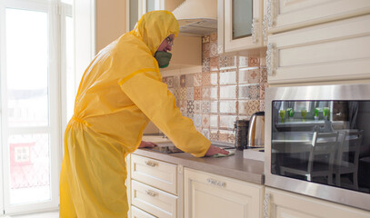 a man in protective special clothing cleans and performs sanitary cleaning in the kitchen in the apartment.