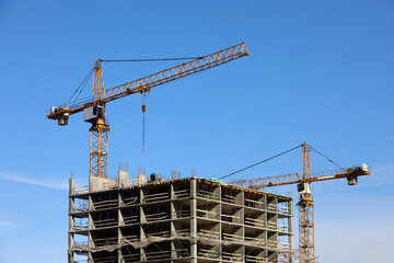 Construction tower cranes above unfinished residential building on blue sky background. Housing construction, apartment block