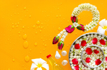 Songkran festival background with jasmine garland, flowers in water bowls, scented water and marly limestone put on clear mirror that have wet yellow background below.