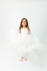 Fototapeta na wymiar A six-year-old girl in a white dress posing in the studio on a white background