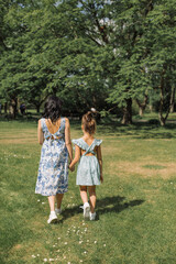 Obraz premium Young mother walking with her little girl in floral dress on a sunny day, having fun in the park.