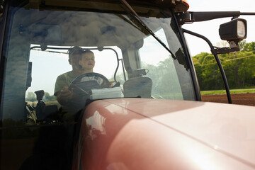Work begins early on the farm. Shot of a young boy sitting with his dad inside the cab of a modern...