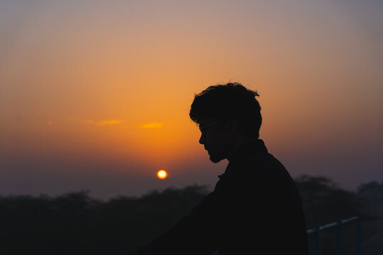 Silhouette of a young boy wearing specs enjoying the beautiful sunset.
