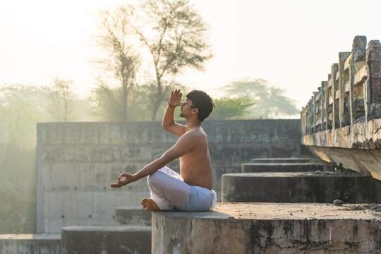 Young indian boy doing anulom vilom yoga while wearing a white dhoti early in the morning. Health and meditation concept. Copyspace for graphics.