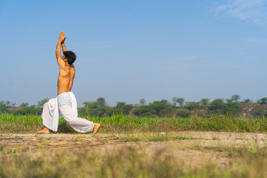 Young indian boy working out in the fields, boy doing yoga wearing a white dhoti in the green fields.