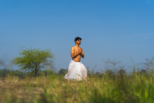 Young indian boy working out in the fields, boy doing yoga wearing a white dhoti in the green fields.