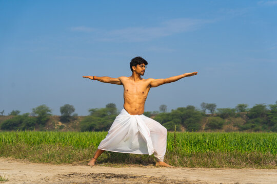 Young indian boy working out in the fields, boy doing yoga wearing a white dhoti in the green fields.