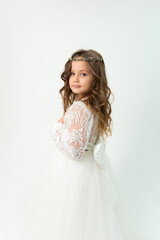 A little girl in a white dress with a tiara on her head posing in the studio