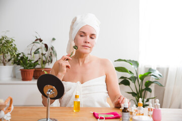 smiling woman 35 year plus in the towel using a stone face roller for facial massage.  Cosmetic...