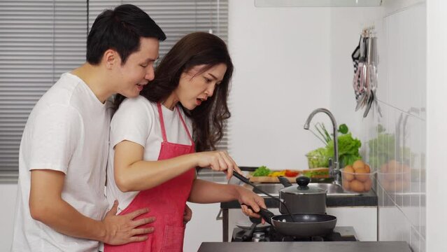 shocked young couple cooking and preparing food in the kitchen at home. man in hugging woman
