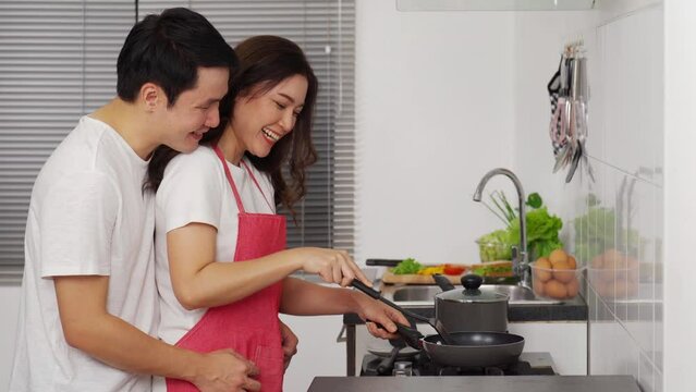 happy young couple cooking and preparing food in the kitchen at home. man in hugging woman