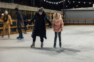Obraz premium mother and daughter skate on the ice rink in the evening