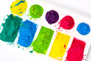 Multicolored holi paints in a palette on a white background from above close-up . High quality photo
