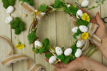 Obraz na płótnie Canvas hands holding easter diy wreath of vines, eggs,stabilized moss,primrose flowers. Materials for making around.