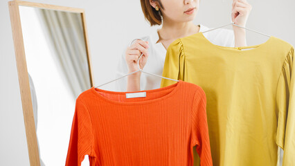 鏡の前で服選びをしている若い女性　ファッションイメージ