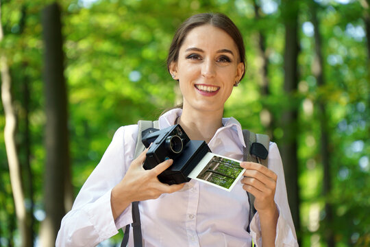 Young woman hiking in forest and taking photo with instant camera