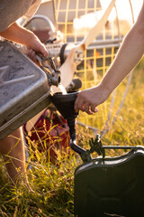 Close-up of male hands pouring gasoline from one canister to another using a plastic funnel. Fuel...