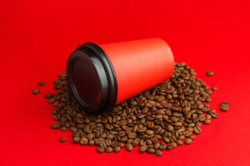 Takeaway red paper coffee cup with black cap lie on roasted beans at red background. Mock up