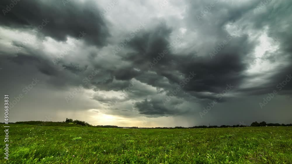 Poster black storm clouds blowing over the green field in timelapse with the view of forest trees in the sp