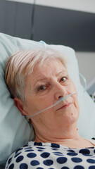 Portrait of elder patient with oxygen tube laying in hospital ward bed. Woman with illness looking...