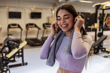 Shot of an attractive young woman taking a break from her workout in the gym. Happy athletic woman with the towel and listening music while exercising in a gym. People, sport and fitness concept