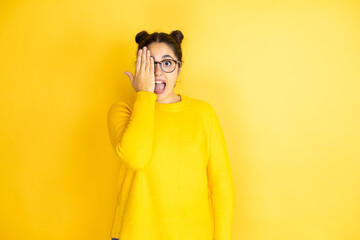 Young beautiful woman wearing casual sweater over isolated yellow background covering one eye with...