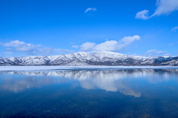 鏡の湖に反射する青空と雪山。冬の北海道の屈斜路湖。