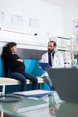 Specialist examining woman expecting baby in maternity cabinet, people talking about pregnancy. Pregnant patient receiving medical advice and support from doctor at prenatal checkup visit.