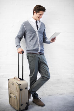 Booking a flight online. A handsome young nerd with luggage working on his tablet.