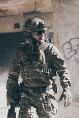 A bearded soldier in a special forces uniform walks through an abandoned building after a...