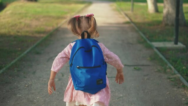 back to school. a little girl with a backpack runs through the green park to school along the path. education kid dream concept. a small child with a backpack back view sun runs the park to school