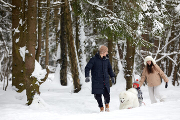 Fototapeta na wymiar Family of mother, father and son having fun in snowy winter wood with cheerfull pet dog.