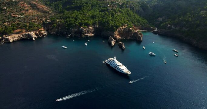 Luxury Super Yacht and speedboats in Mediterranean with view of mountains and beach. Aerial orbit shot