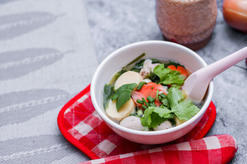 Boiled tofu and minced pork served in white cups with red checkered saucers placed on a white table.