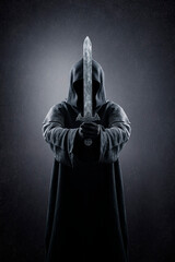 Warrior with hooded cape and medieval sword over dark misty background