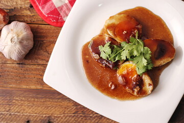 Egg with Tamarind Sauce in a white plate served on a wooden table with coriander sprinkles, is a popular local dish that Thai people eat.