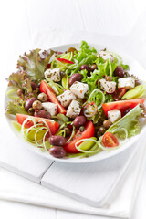 Healthy salad with feta cheese, various olives, leek and tomatoes. White wooden background. Close up.